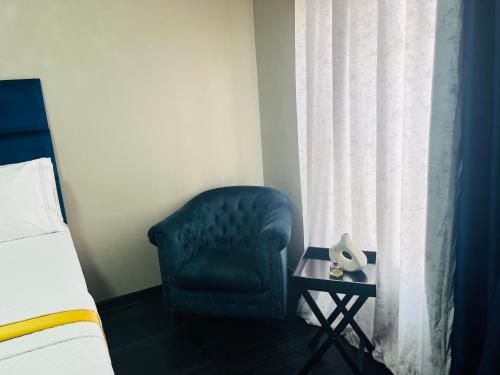 a bedroom with a blue chair next to a window at Shiloh Tlokweng in Gaborone