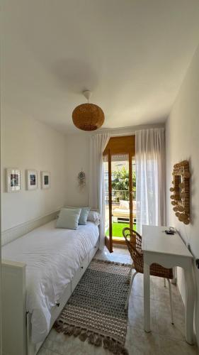a white bedroom with a bed and a desk and a window at Casa de playa in Roda de Bará