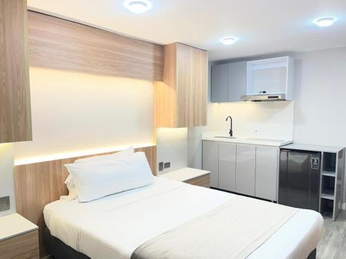 a bedroom with a white bed and a kitchen at ApartaSuite City Bog Usaquén in Bogotá