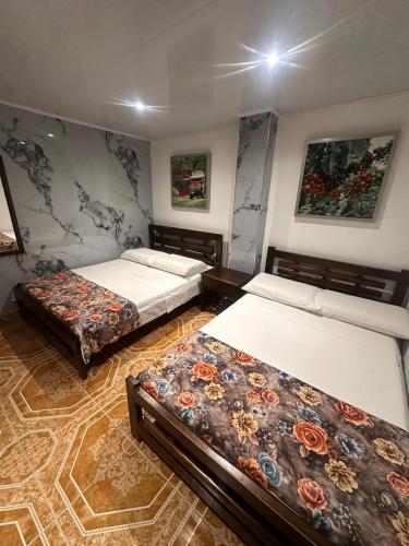 a room with three beds and paintings on the wall at Hotel Confortel in Armenia