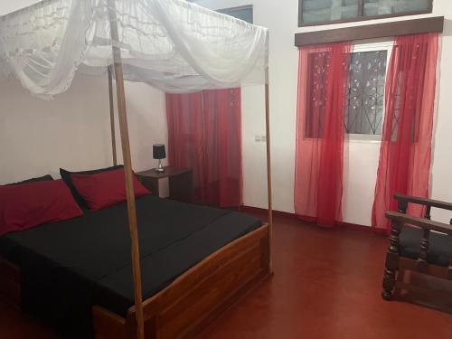 a bedroom with a canopy bed with red curtains at Villa Cali PASO in Sambava