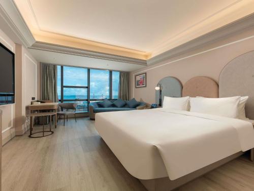 a bedroom with a large white bed and a living room at Mercure Danzhou Yangpu Seaview in Dongshan