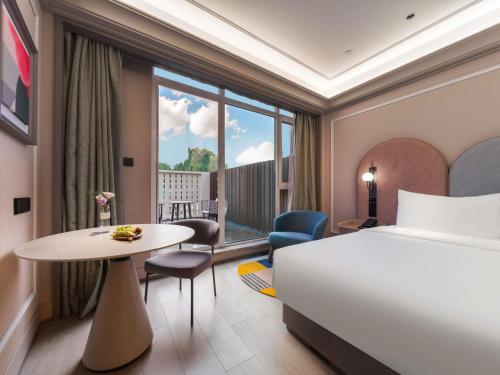 a hotel room with a bed and a table and a window at Mercure Qingdao Coast in Qingdao