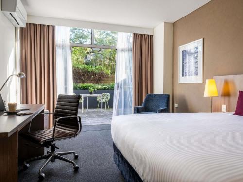 a hotel room with a bed and a desk and chairs at Mercure Sydney St Leonards in Sydney