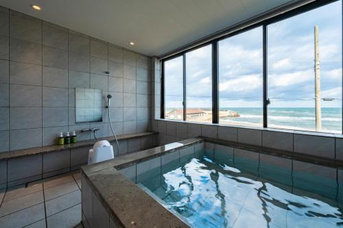 a bathroom with a tub with a view of the ocean at KITAMAE BASE Kaga Hashitate in Kaga