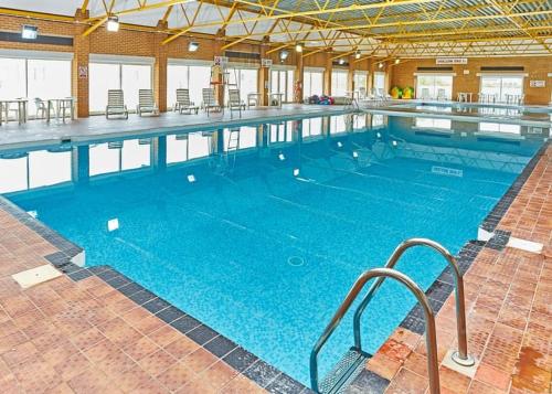 a large swimming pool with blue water in a building at Beach Retreats, Romney Sands, Parkdean Resorts in Greatstone