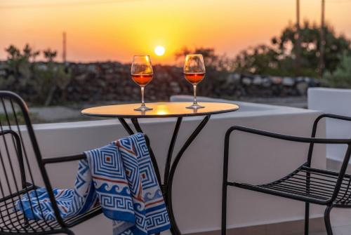 two glasses of wine sitting on a table with the sunset at Theophrasti Suites in Foinikiá