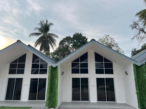 a white house with large windows and a palm tree at Gopeng Tiny House CUCHU in Gopeng