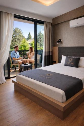 a bedroom with a bed and a man and woman sitting on a balcony at stay on hotel in İzmir