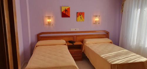 two beds in a room with purple walls at Hostal Restaurante Carolina in Pedrosillo el Ralo