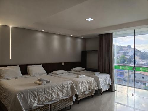 two beds in a bedroom with a large window at Hotel Esmeralda Verde in Teófilo Otoni