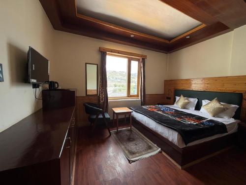 a bedroom with a bed and a window and a television at The Juniper Ladakh Guest House in Kargil