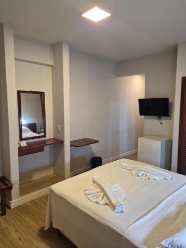 a room with a bed with a mirror and a television at Thanharu Praia Hotel in Anchieta
