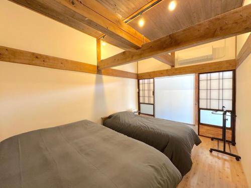 two beds in a room with wooden ceilings and windows at Ango KIKAIJIMA in Onozu