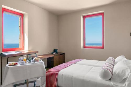 a bedroom with a bed and a table and two windows at Hotel Boutique Faro Silleiro in Baiona