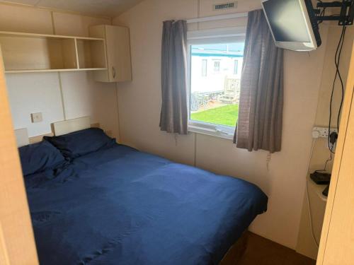a small bedroom with a blue bed and a window at Seaside Getaways Caravan Hire in Chapel Saint Leonards
