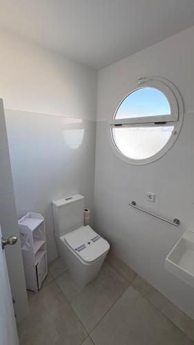 a white bathroom with a toilet and a window at Hostal Noray in Punta Prima