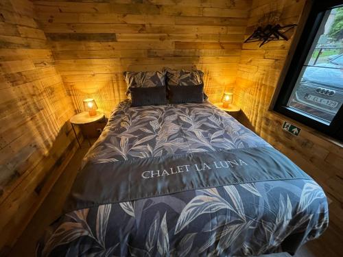 a bed in a wooden cabin with two lamps on tables at La Luna in Lanaken