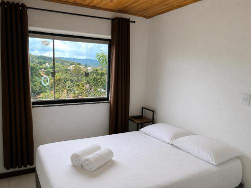 a bedroom with a white bed and a large window at Casa com 2 suítes em Lavras Novas in Ouro Preto