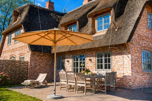 a table with chairs and an umbrella in front of a house at Haus Lang Libben in Archsum