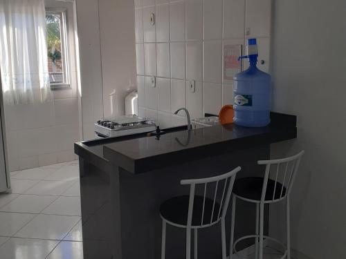 a kitchen with a counter with two stools and a bottle of water at Apartamento 204 com vista da piscina e mar in Piúma