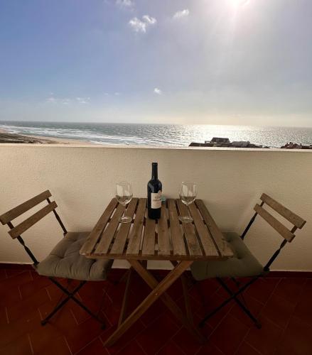 a wooden table with a bottle of wine and two glasses at Face a l'océan, vue panoramique, 3 min a pied de la plage, Praia da areia branca in Praia da Areia Branca