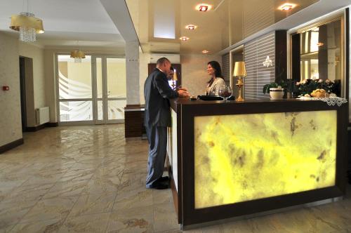 two people standing at a counter in a lobby at Hotel z Sanatorium Uzdrowiskowym Knieja Spa&Wellness in Supraśl