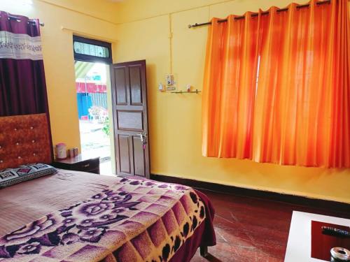 a bedroom with a bed and a window with orange curtains at ADROSE COTTAGESs in Colva