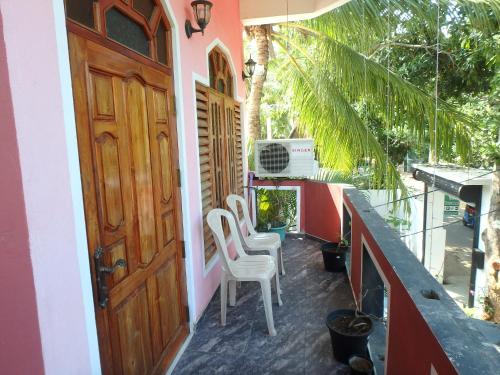 eine Veranda mit weißen Stühlen und einer Holztür in der Unterkunft K Holiday in Tissamaharama