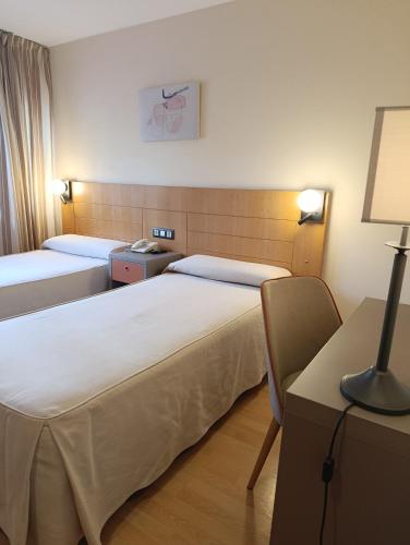 a hotel room with two beds and a desk with a lamp at Hotel Villa de Zaragoza in Casetas