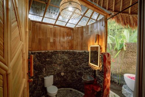 a bathroom with a toilet and a stone wall at Bambu Teras Viewpoint in Karangasem