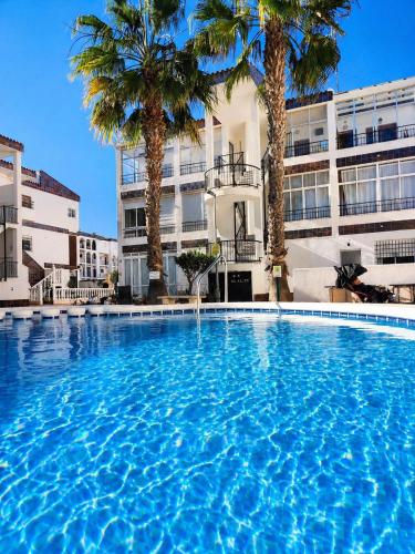a large swimming pool with palm trees in front of a building at Caballito del Mar apartment in Punta Prima