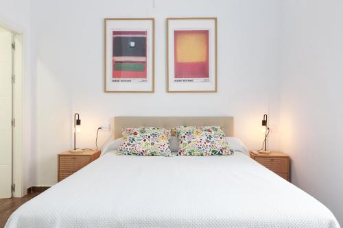 a bedroom with a white bed with two pictures on the wall at Duplex con vistas en el centro de Aracena in Aracena