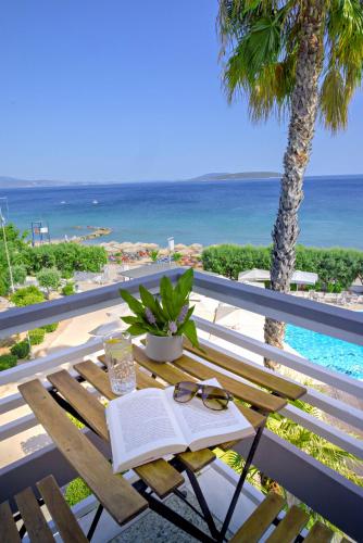 a table with a book and glasses on a balcony with the beach at The Grove Seaside Hotel in Drepana