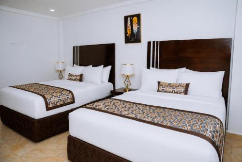 Zwei Betten in einem Hotelzimmer mit weißen Wänden in der Unterkunft Sinkor Palace Hotel in Monrovia