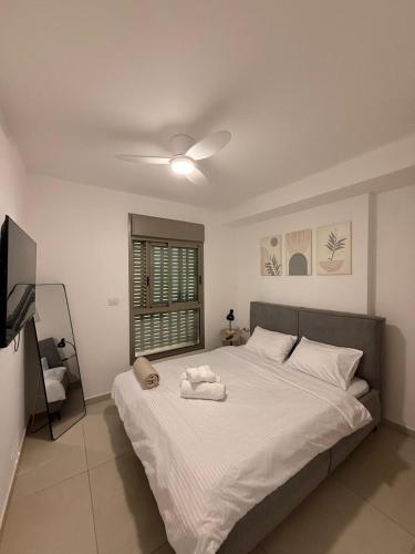 a bedroom with a large white bed with a ceiling fan at Sunset suite - step from the beach in Ashkelon