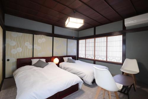 a bedroom with two beds and a chair and two windows at 氷見のお宿むすびえ 旧やわや 1日1組1棟貸し in Himi