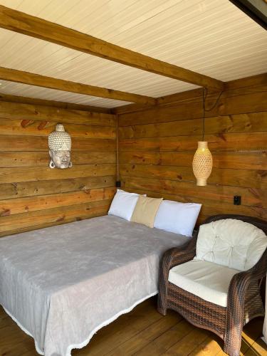 a bed and a chair in a room with wooden walls at Suítes Âncora Praia do Rosa in Imbituba