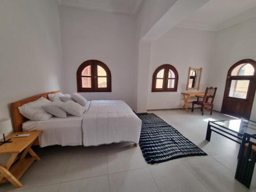 a bedroom with a bed and a table and two windows at Maison Sakeena in Saint-Louis