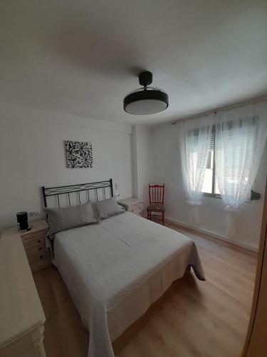 a white bedroom with a bed and a window at Alojamiento El Sevillano in Cullera