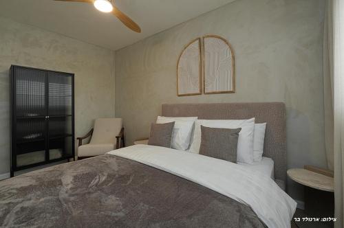 a bedroom with a large bed and a chair at Shilo Boutiqe Suites in Mishmār Hāyardin