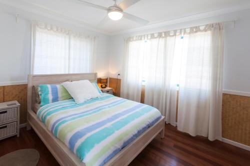 a bedroom with a bed with a striped blanket and windows at White Waves on the Beach in Hastings Point
