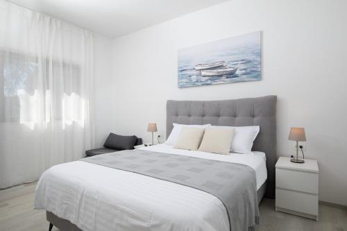 a white bedroom with a large bed and a chair at Apartments Dadic with parking & playground in Medulin