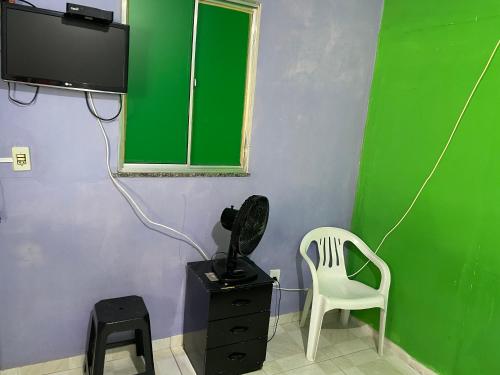 a room with a green wall with a chair and a television at Hospedagem da Bela Quarto 4 Banheiro compartilhado in Caparaó Velho