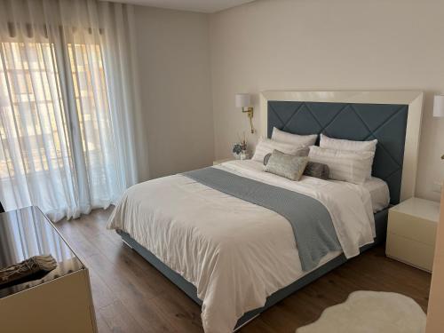 a white bedroom with a large bed with a blue headboard at Carrousel Atlantic View in Rabat