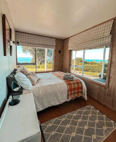 a bedroom with a bed with windows and a table at Patons Rock Cutie in Rangihaeata