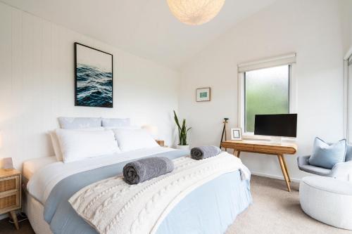 a white bedroom with a large bed and a chair at Surf Haven in Lorne