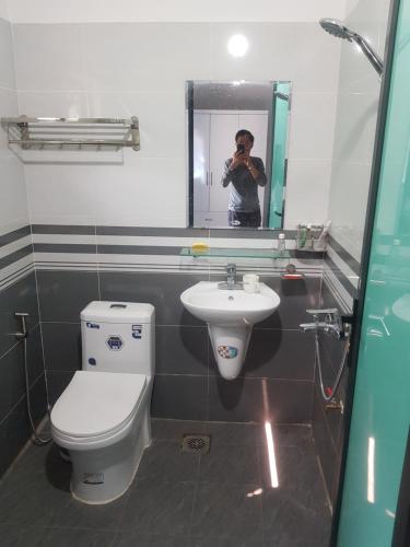 a man taking a picture of a bathroom with a toilet and sink at Nhà nghỉ My Home in Mộc Châu