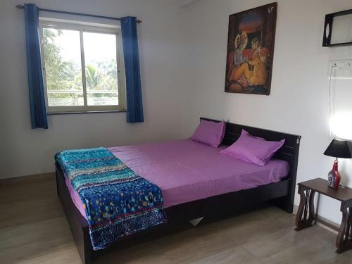 a bedroom with a bed with purple sheets and a window at Ocean Shores Hospitality in Candolim