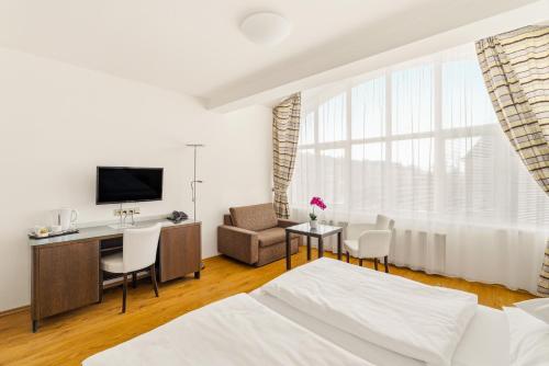 a room with a bed and a desk and a tv at Hotel Trinity in Olomouc